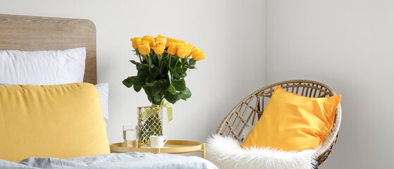 Vase with beautiful yellow roses on bedside table in room