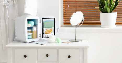 Small cosmetic refrigerator with products and mirror on dressing table in bathroom