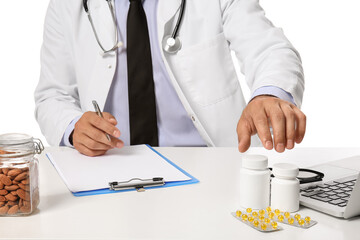 Male doctor with vitamins writing in clipboard at table on white background
