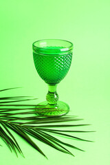Glass of tasty cocktail and palm leaf on green background