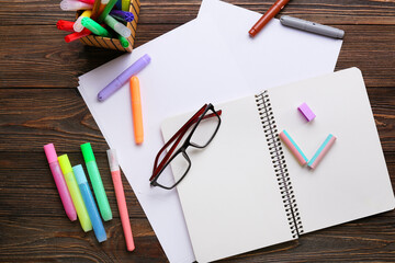 Paper sheets with notebook, felt-tip pens and eyeglasses on dark wooden background