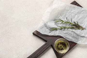 Board with baking paper, rosemary and bowl of oil on light background
