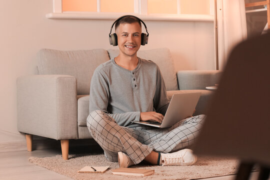 Young man with headphones and laptop studying online at home late in evening
