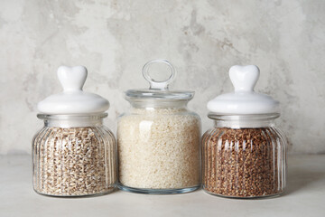 Glass jars with cereals on light background