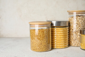 Glass jars with different cereals on light background