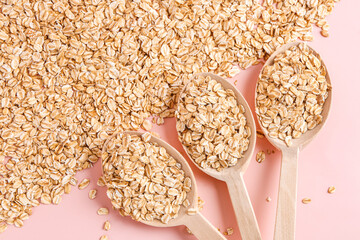 Wooden spoons with raw oatmeal on pink background, closeup