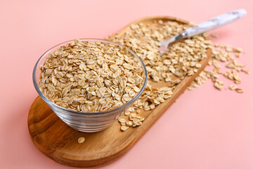 Wooden board with bowl of raw oatmeal on pink background, closeup