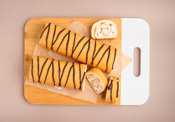 Wooden board with delicious sponge cake rolls on color background
