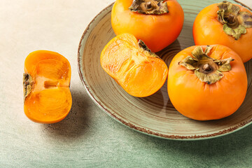 Plate with fresh persimmons on grunge background, closeup