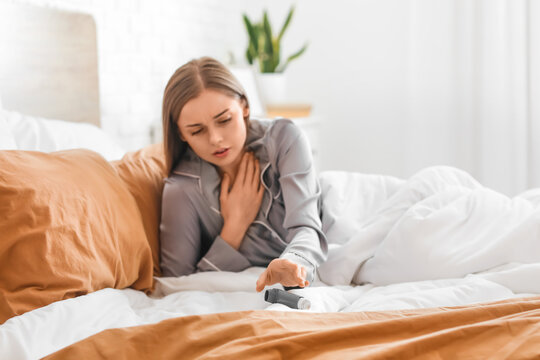 Sick young woman with inhaler in bed