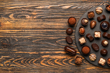 Slate board with chocolate candies on wooden background