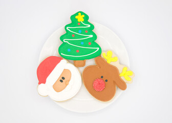 Top view flat lay of fancy decorated sugar cookies in Christmas shapes. Santa, Tree and Reindeer on a round porcelain plate on off white background.