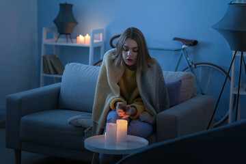 Young woman warming hands near burning candles at home during blackout
