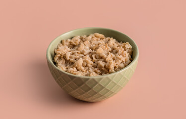 Bowl with tasty oatmeal on pink background