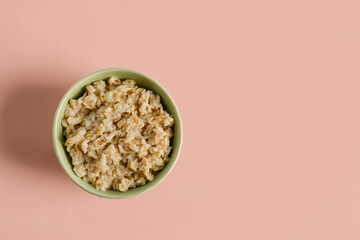 Bowl with tasty oatmeal on pink background