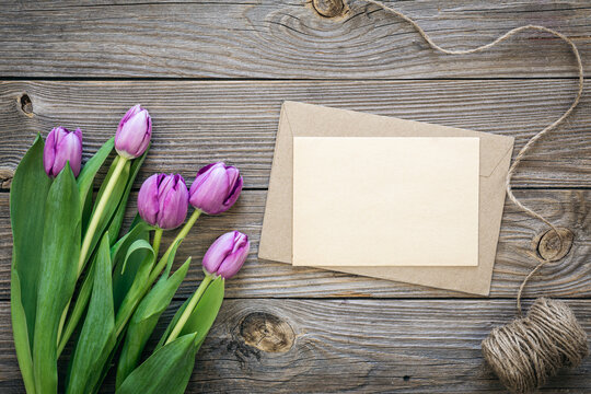 Bouquet of purple tulips and blank greeting card on wooden background, top view, copy space.