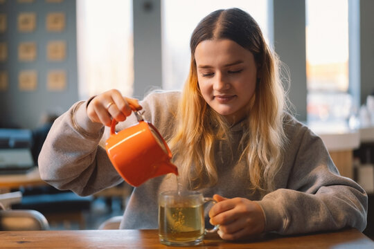 Portrait of a joyful teengirl enjoying a cup of tea at cafe. Smiling beautiful girl drinks hot tea in winter. Teengirl drinking hot tea. Cafe city lifestyle. Colorful portrait of happy pretty girl