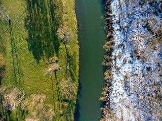 Aerial view. The river as seen from above. Winter, spring. Half and half. Landscape, trees, snow, water, shadows.