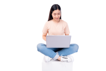 Happy young asian woman sitting on white chair with legs crossed and using laptop computer on light pink background copy space Full body young smiling happy female wearing t shirt and jeans lifestyle