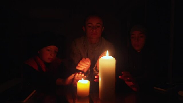 Family sitting around a table lit by candlelight during an electrical power cut.