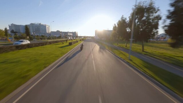 Biker black leather outfit riding custom motorbike on road traffic touristic sunny city. Cinematic aerial FPV sport drone chase shooting follow motorcycle surrounded town architecture building and car