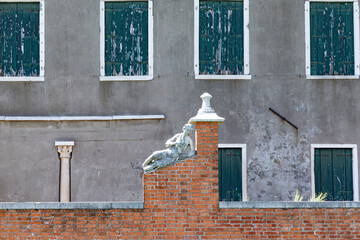 historic marble figure of a beautiful woman at a fence with closed shutter in background at island of Burano, Venice