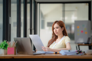 Stressed and serious Asian businesswoman or financial consultant reading a financial report.