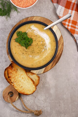red lentils soup puree in dark bowl with bread on grey marble table