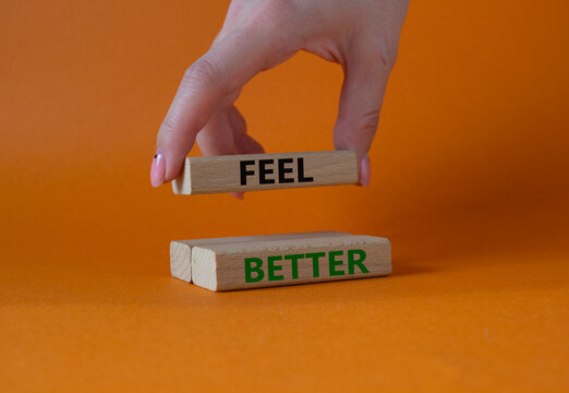 Feel better symbol. Wooden blocks with words Feel better. Businessman hand. Beautiful orange background. Business and Feel better concept. Copy space.