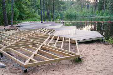 Walking area on screw piles, wooden frame, plastic terrace board on pond shore in park, construction site