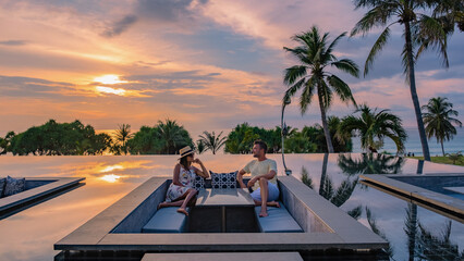 couple watching the sunset in an infinity pool on a luxury vacation in Thailand, man and woman...