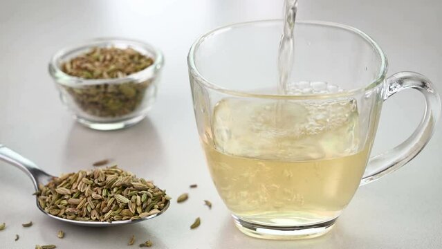 Serving fennel seed water in a glass cup with fennel seeds in the background.