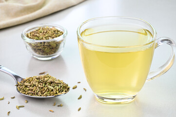 Fennel seed water in a glass cup with fennel seeds in the background.
