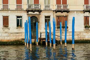 empty pier with typical blue venetian posts in front of the entrance of a house on the canal