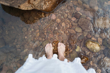 Selfie of female feet in sea water on a pebble shore in summer, top view and copy space.