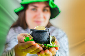 Smiling irish girl in Leprechaun costume holds pot with gold coins.