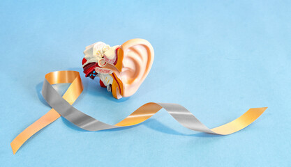 Gold silver ribbon with anatomical ear model, for hearing disorders illness awareness.