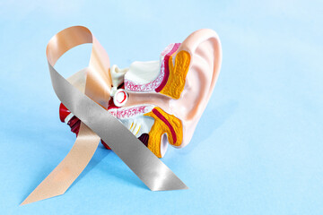 Gold silver ribbon with anatomical ear model, for hearing disorders illness awareness.