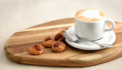 Cappuccino coffee in white cup on wood board with almond cookies