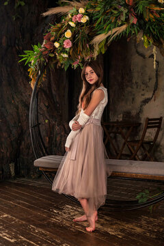 Teenager girl in light pink dress barefoot posing in mystery decorated room with flowers indoors. Fashionable smile teen princess looking at camera. Fantasy art photo, fairy tale concept. Copy space
