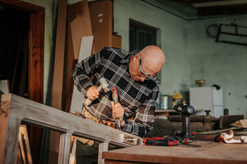 Senior carpenter using chisel and hammer in workshop