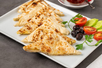Traditional Turkish flatbread or Gozleme with tomatoes, olives and tea on dark stone table