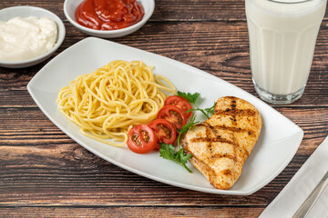 Spaghetti and grilled chicken on a white porcelain plate with buttermilk and sauces on wooden table