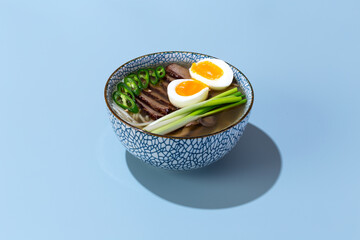 bowl of ramen with beef and eggs on blue background