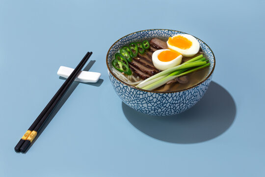 bowl of ramen with beef and eggs on blue background