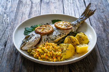 Roast sea bream with potatoes and vegetables on wooden table
