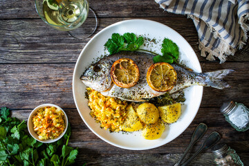 Roast sea bream with potatoes and vegetables on wooden table
