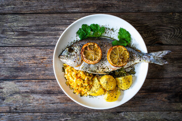 Roast sea bream with potatoes and vegetables on wooden table

