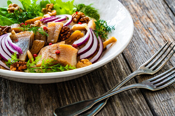 Marinated herrings with delicacies, walnuts and fresh vegetable leaves on wooden table
