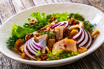 Marinated herrings with delicacies, walnuts and fresh vegetable leaves on wooden table
